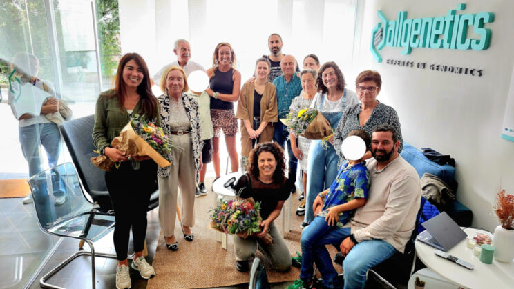 The image shows Dr Verónica Rojo, Dr Belén Carro, and Dr Neus Marí-Mena with their families at the AllGenetics' headquarters.